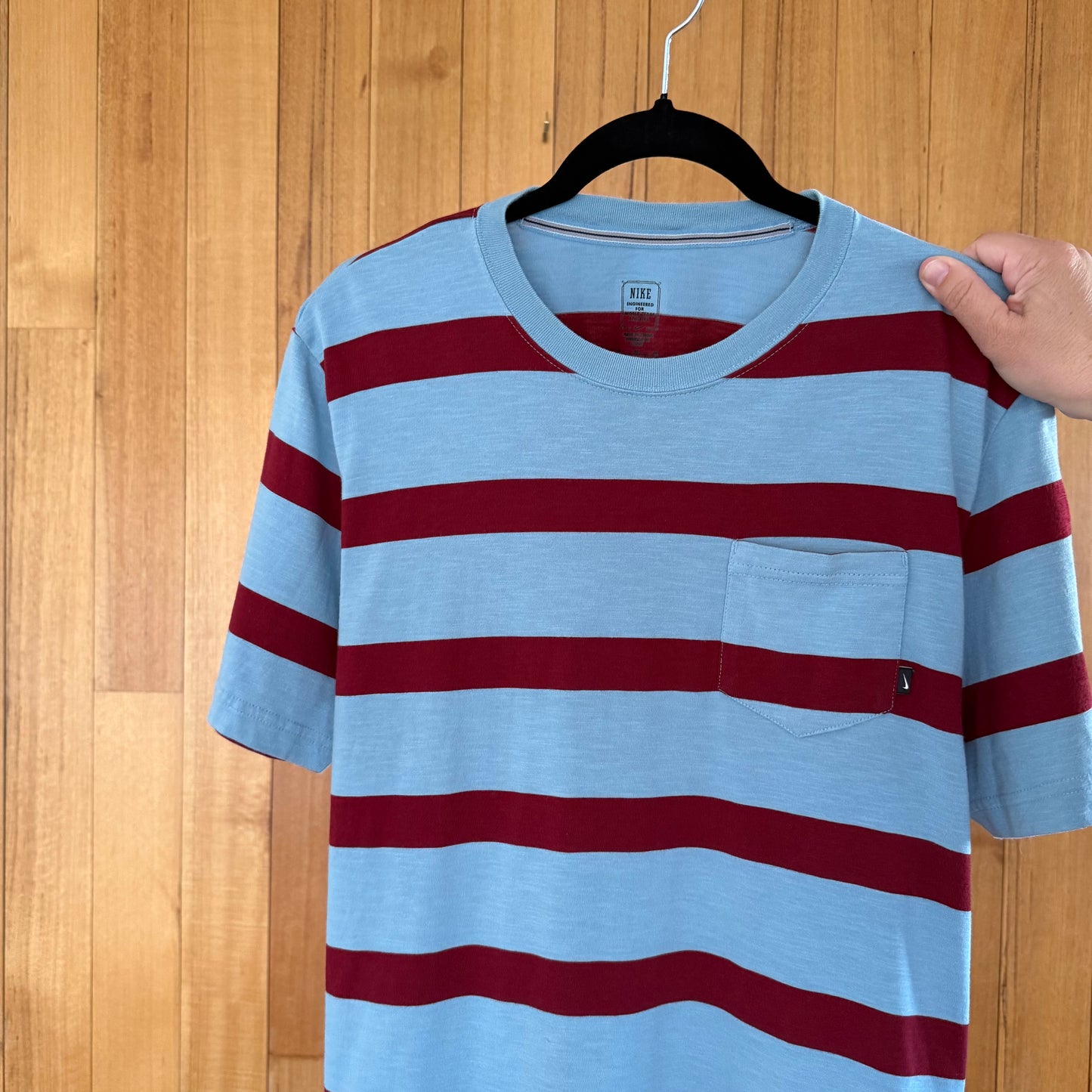 Close-up of chest pocket detail on light blue Nike Action Sports striped t-shirt